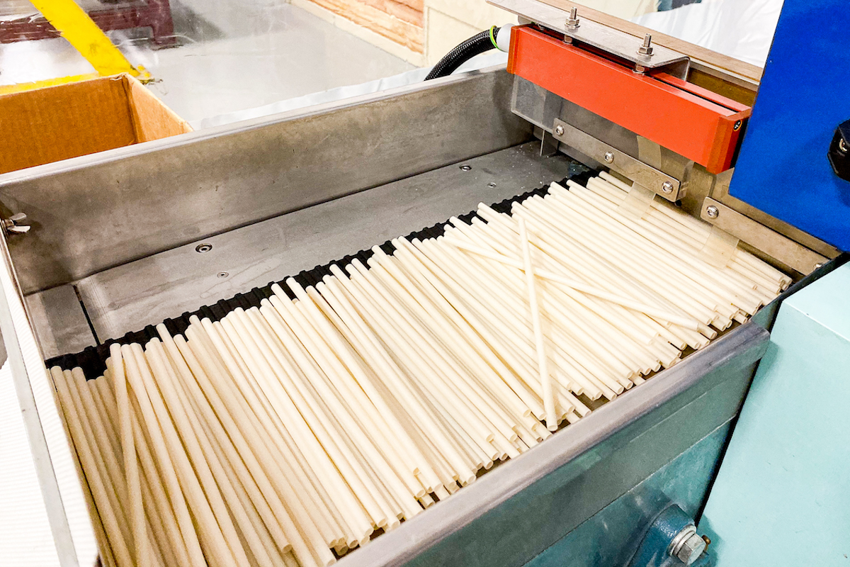 Compostable straws move through a machine during production phases at UrthPact's custom compostable goods production facility.